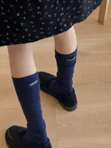 Detail shot of navy blue mid-calf socks with letter patch label paired with black loafers.
