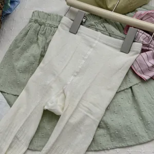 Close-up detail of white ribbed knit pantyhose paired with a green skirt on a hanger.