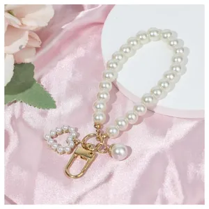 Detail shot of a white imitation pearl keychain wrist strap with a cute heart charm and gold hardware.