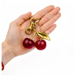 Close-up of cute glitter red cherry keychain and bag charm with gold metal hardware detailing.