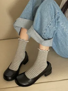 Close-up detail of women gray striped socks with cute ruffled edge worn with black shoes.