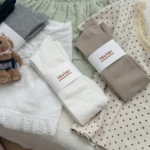Detail shot of casual ribbed over-the-knee socks with paper band packaging in neutral tones.