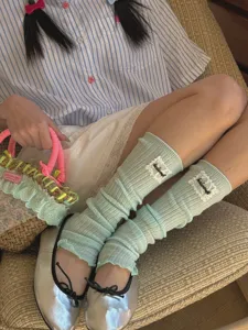 Close-up detail of soft knit leg warmers in pastel green with cute lace patch design.