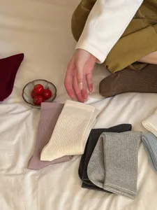 Detail shot of solid color ribbed mid-tube socks in various soft tones on a cozy white bed.