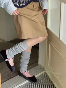 Dettaglio in primo piano di scaldamuscoli in maglia grigia con classiche scarpe Mary Jane.