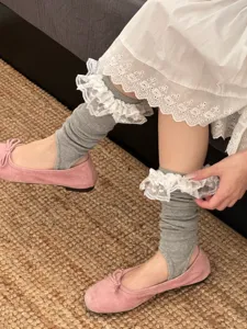 Detailed view of grey stirrup socks with white lace trim, worn with pink flat shoes.