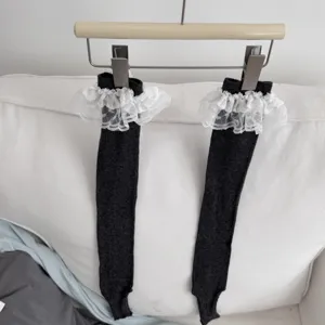Dark grey stirrup socks detail with white lace ruffle trim hanging on wooden hanger close up