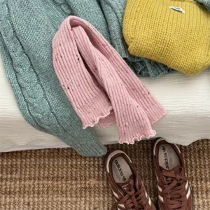 Dettaglio di scaldamuscoli in maglia rosa con macchie colorate e bordo con volant.