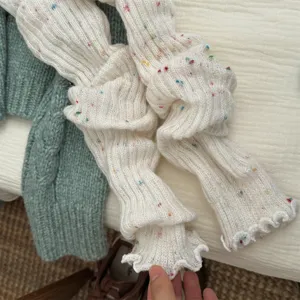 Primo piano di scaldamuscoli in maglia bianca con punti colorati coriandoli e orlo volant.