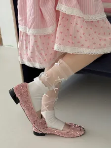 Detailopname van doorschijnende mesh beenwarmers met strikken en witte sokken.