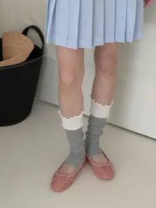 Close-up detail of layered ruffle leg warmers paired with pink ballet flats and skirt.