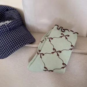 Close-up detail of light green ruffle socks with cute brown bow pattern, soft breathable fabric.