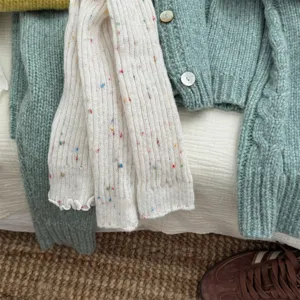 Primo piano dettagliato di scaldamuscoli in maglia bianca con pois colorati invernali.