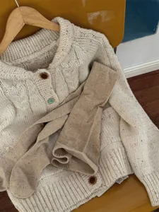 Detailed shot of cozy cable-knit cardigan and textured tights, warm autumn style.