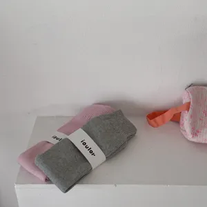 Dettaglio di scaldamuscoli in maglia, calze rosa e grise morbide con confezione in fascetta di carta.