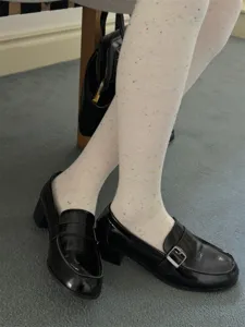 Close-up of white speckled tights paired with black patent leather loafers for women.