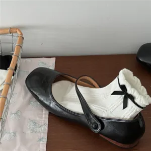 Primo piano di scarpe Mary Jane nere abbinate a calzini bianchi con volant e fiocco.