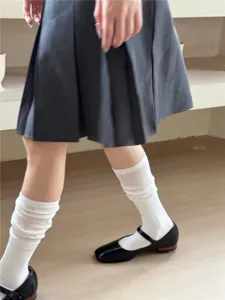 Detailed shot showing the white slouch socks paired with a pleated skirt and Mary Jane shoes.