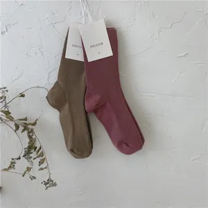 Gros plan de chaussettes montantes en tricot unicolore accrochées sur un mur blanc.