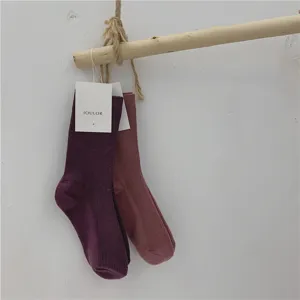 Gros plan de chaussettes mi-hautes unies minimalistes suspendues sur une tringle en bois rustique.