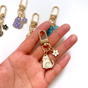 Cute white cat keychain detail shot, enamel kitty pendant with flower charm, metal accessory.