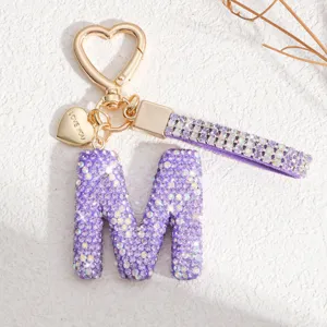 Gros plan détaillé du porte-clés lettre M en strass violet scintillant avec mousqueton cœur.