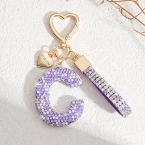 Gros plan détail d'un porte-clés lettre C en strass violet scintillant avec pendentif cœur.