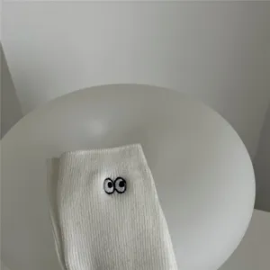 Gros plan de chaussettes mi-hautes blanches en coton avec jolis yeux brodés noirs.