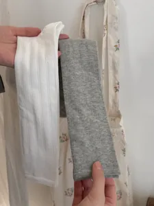 Detail shot showing white ribbed and grey calf socks held by hand against a floral background.
