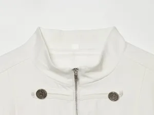 Nahaufnahme des weißen Stehkragen-Blazers mit Metallreißverschluss und dekorativen Knöpfen.