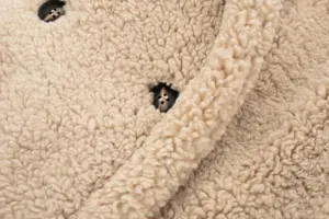Beige sherpa fleece winter coat fabric detail, soft fuzzy texture with dark buttons close up