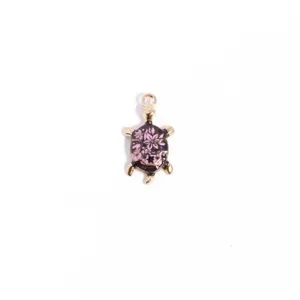 Detailed close-up of a metal turtle charm with floral enamel shell, gold-toned part.