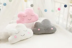 Close-up shot of cute cloud plush pillows in pink and grey with sweet embroidered faces.