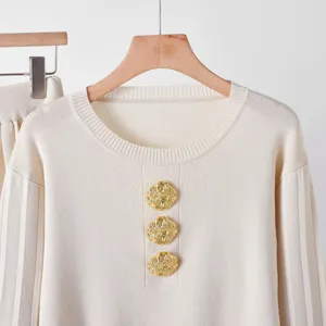 Détail élégant de haut en tricot crème avec boutons dorés texturés et col rond chic.