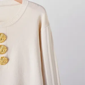 Gros plan détaillé du pull en tricot avec des boutons dorés gaufrés et des manches côtelées.
