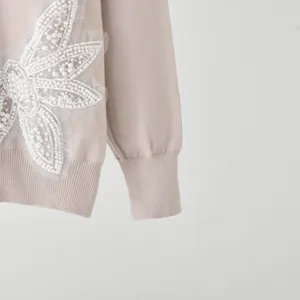 Close-up detail of the stylish knitted sweater featuring exquisite white pearl and lace embroidery.
