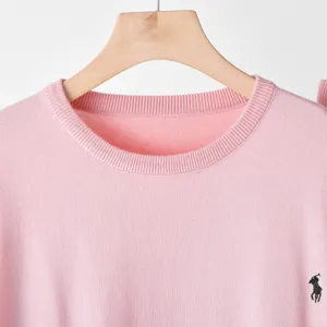 Pink round neck long sleeve knit top with delicate embroidered logo on hem detail view.