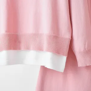 Knit sweater set detail showing pink top with white layered hem and matching knit trousers.