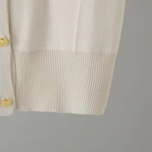 Detailed view of beige knit fabric with elegant gold buttons and ribbed hem texture.