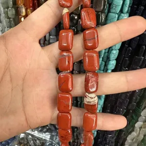Nahaufnahme von natürlichen roten Jaspis-Rechteckperlen in der Hand für DIY-Schmuck