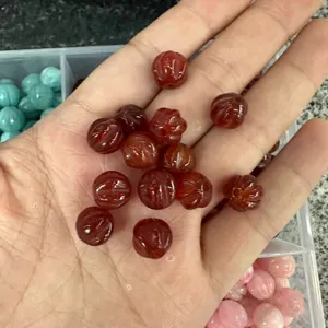 Natural red agate pumpkin-shaped loose beads for DIY jewelry making held in a person's hand