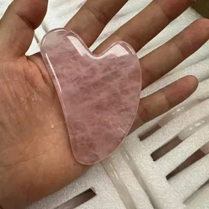 Détail macro d'un outil gua sha en quartz rose en forme de cœur pour massage facial