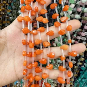 Primer plano de cuentas de piedra natural naranja en forma de gota facetada con agujero horizontal.