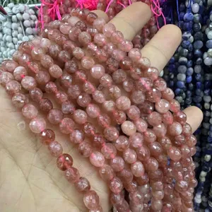 Gros plan de perles de quartz fraise à facettes de 6 mm tenues à la main pour bijoux DIY