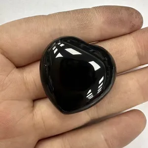 Nahaufnahme eines glatt polierten, herzförmigen schwarzen Obsidiankristalls in einer Handfläche