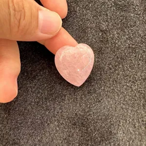 Gros plan d'une pierre d'agate rose en forme de cœur tenue entre les doigts pour la taille