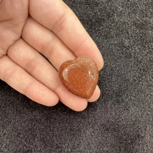 Vue détaillée d'un cabochon en pierre d'or brun étincelant en forme de cœur tenu à la main