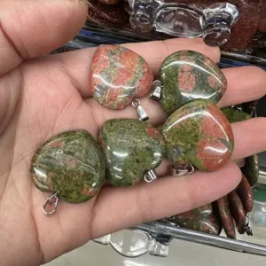 Close-up of heart-shaped Unakite stone pendants held in a hand, showing natural patterns