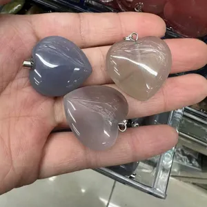 Detailed view of three 25mm heart-shaped natural crystal pendants displayed in hand.