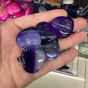 Close-up of hand holding purple striped agate heart jewelry pendants with silver bails